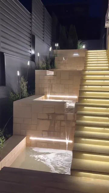 Каскадный водопад из камня и лестница с LED-подсветкой в ландшафтном дизайне участка ночью